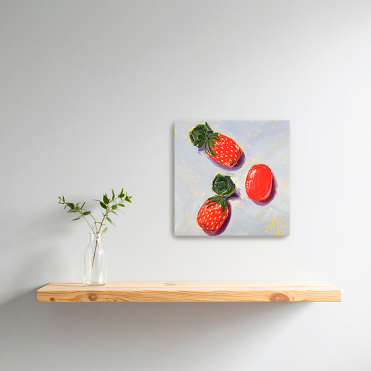 Framed artwork of strawberry candies on a wooden shelf with a vase of greenery.