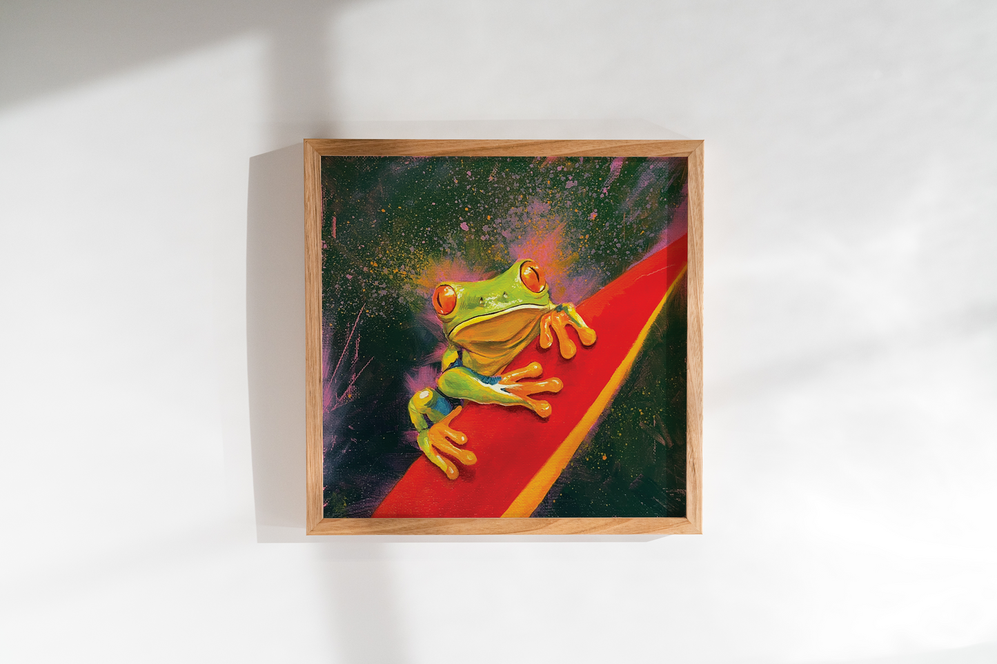 Framed artwork of a colorful frog on a red leaf. Pink and green background.