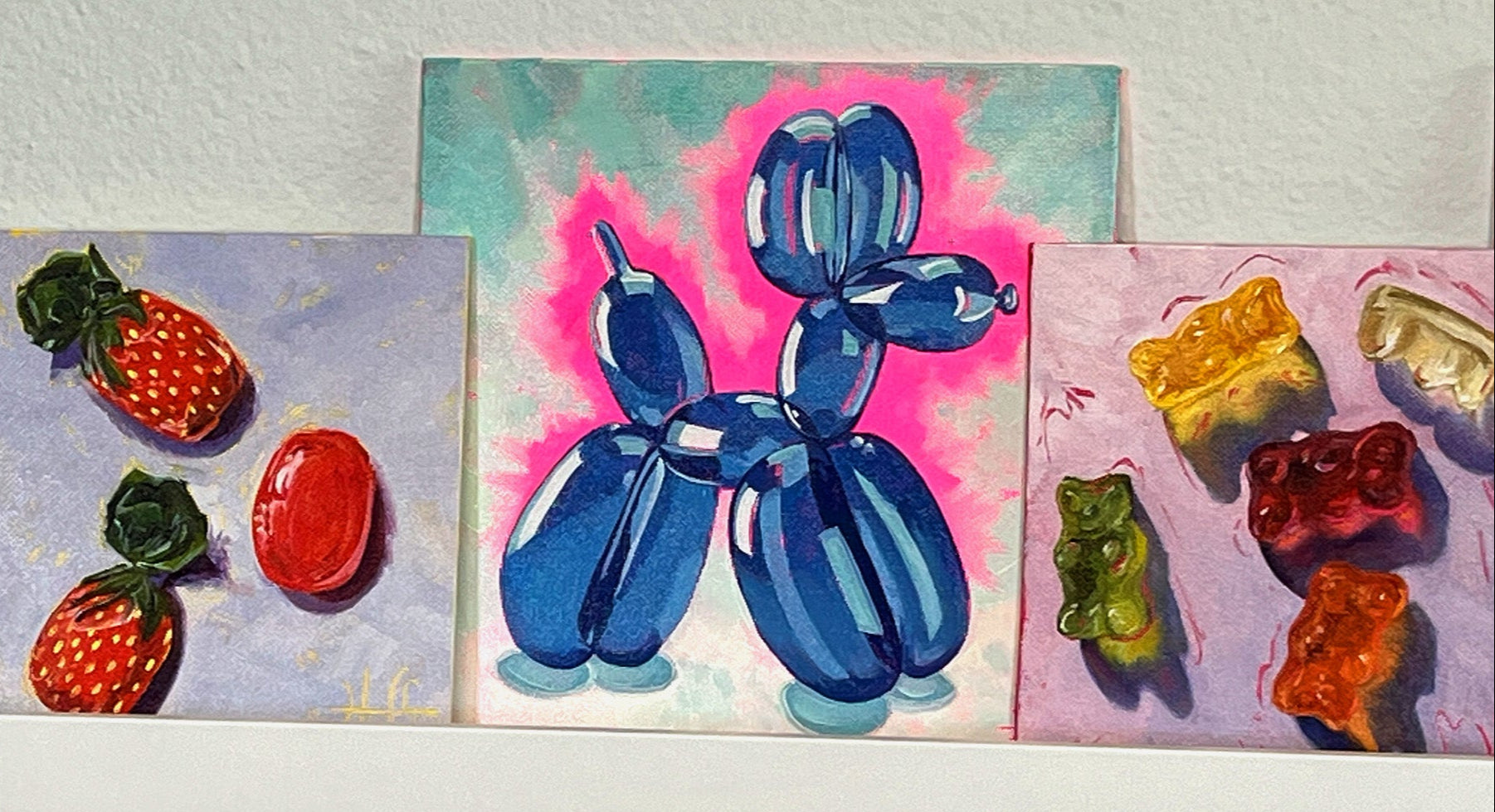 Three colorful paintings of a blue balloon dog, sparkling strawberry candies, and glowing gummy bears on a white surface.