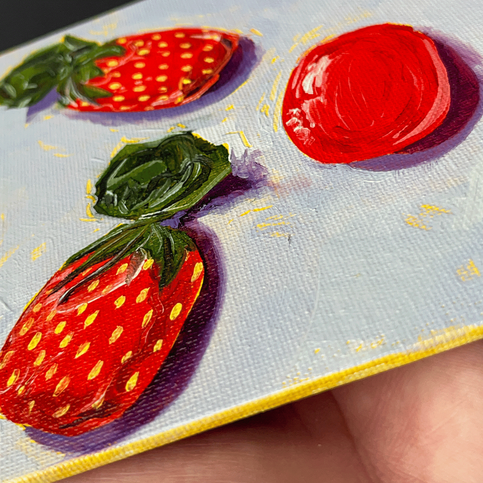 Close-up of a hand holding a small painting of strawberry candies on a textured surface.
