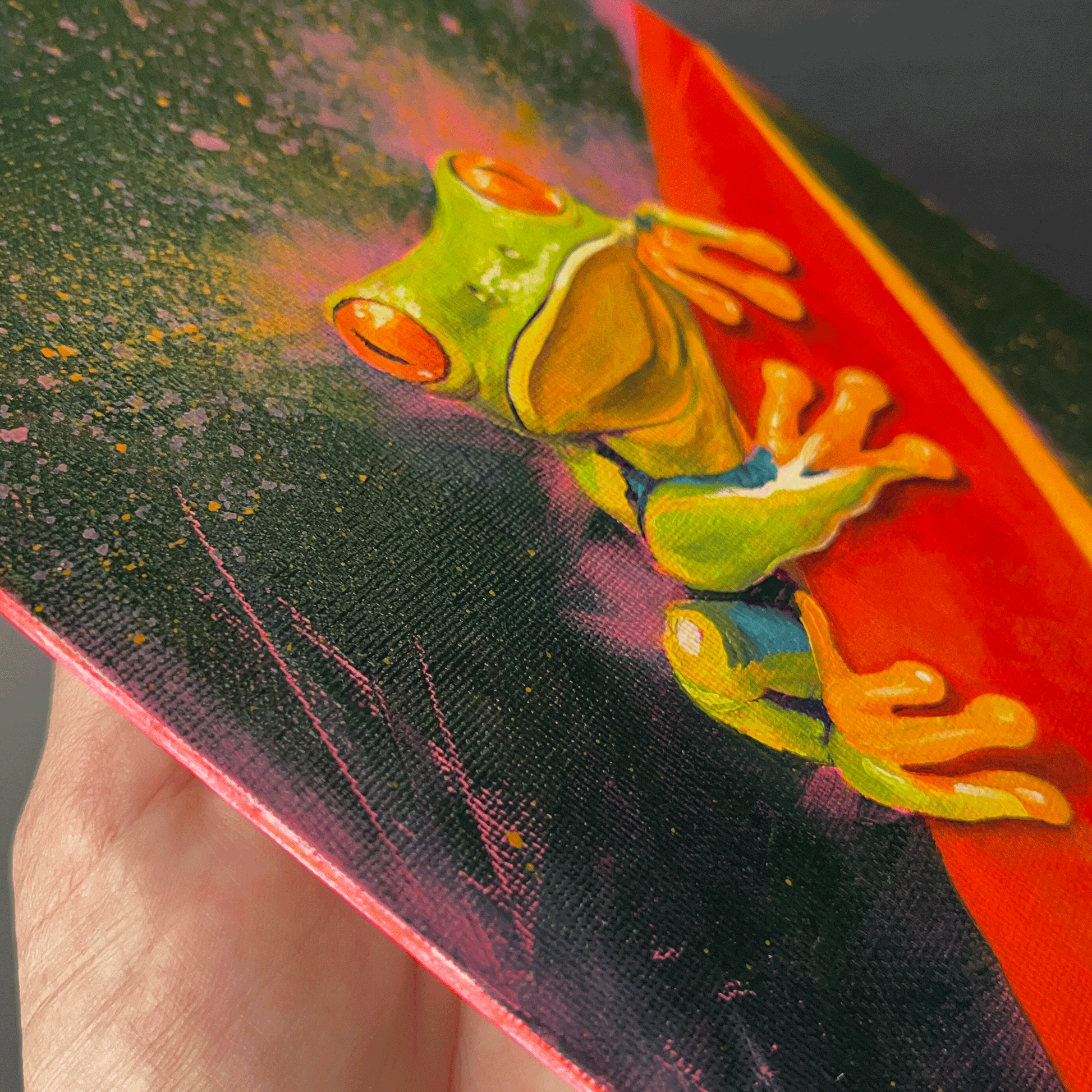 Side view of a pink canvas panel with a green tree frog design on a colorful background.