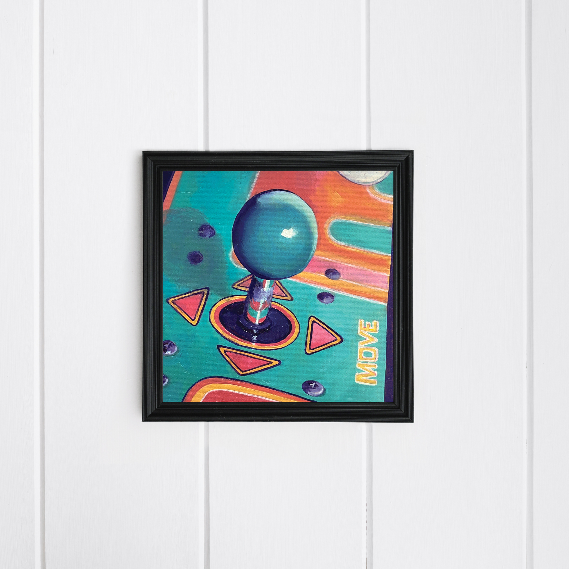 Framed artwork of a joystick on a colorful background mounted on a white wooden panel wall.